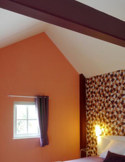 Vue sur une chambre avec un papier peint géométrique prune et rose corail en tête de lit © francois louchet, par CREA DECO, Décoratrice UFDI à Honfleur, Deauville, Caen - 14